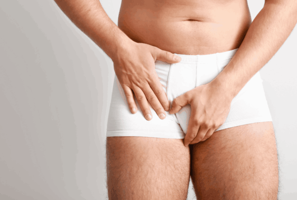 Man in white underwear clutching his groin, suggesting discomfort or pain.