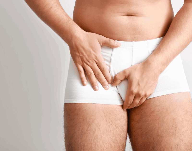 Man in white underwear clutching his groin, suggesting discomfort or pain.